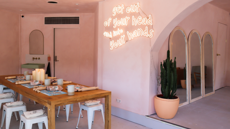 A pink room with a table and neon sign saying; get out of your head and into your hands