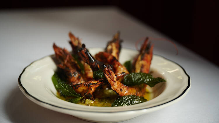 A white table with a white bowl filled with prawns with green sauce 