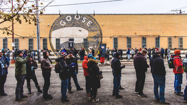 A group of people stand in line in front of the Goose Island 