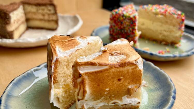 A plate with a lamington covered in torched meringue is cut in half with other lamingtons in the background