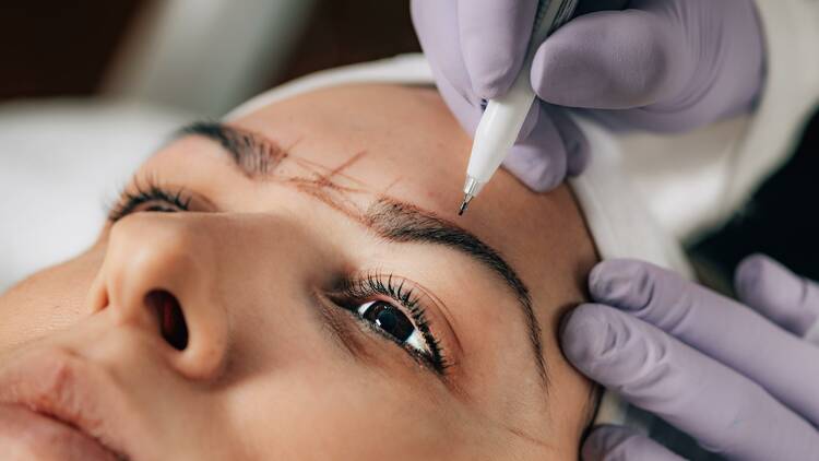 A technician drawing on a woman's eyebrows.