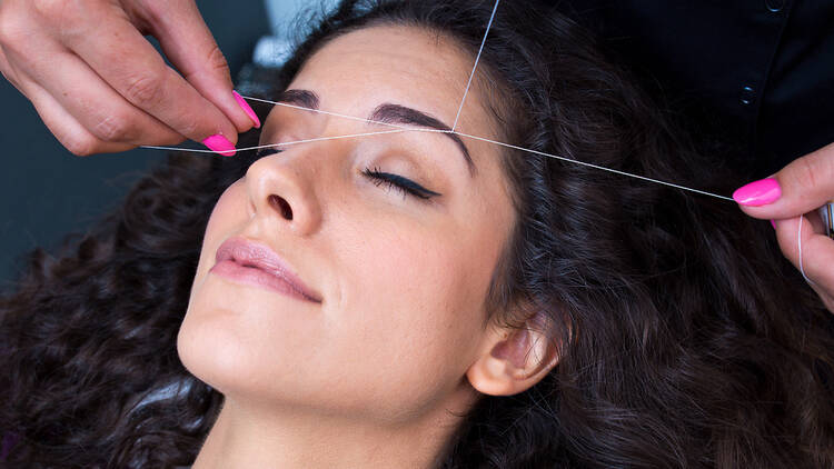 A woman receiving an eyebrow threading treatment.