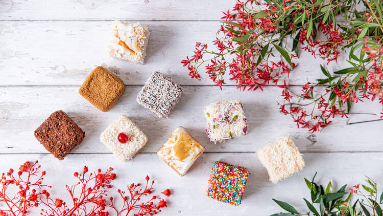 A white table with different lamington flavours and flower branches on the side from a birds eye view