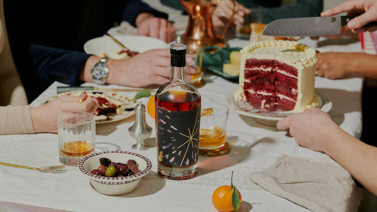 A bottle of Starward whisky is in the middle of table with friends enjoying birthday cake