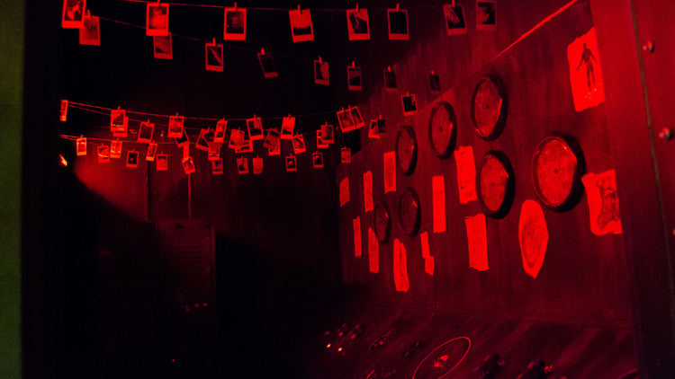 A dark, red-tinged room filled with hanging polaroid pictures.