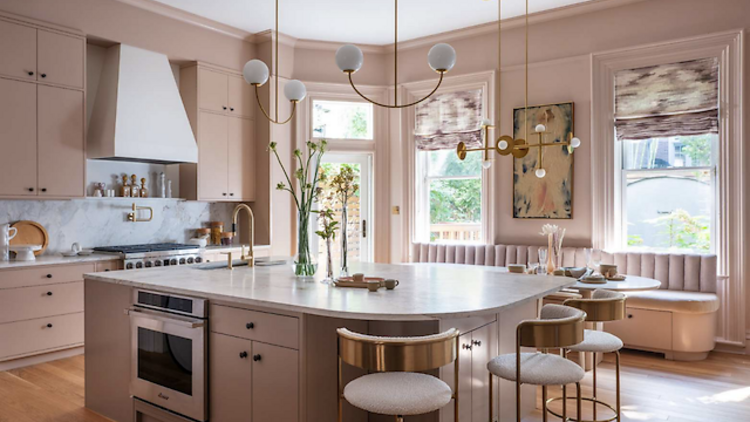 A kitchen with pink cabinetry and large windows. 