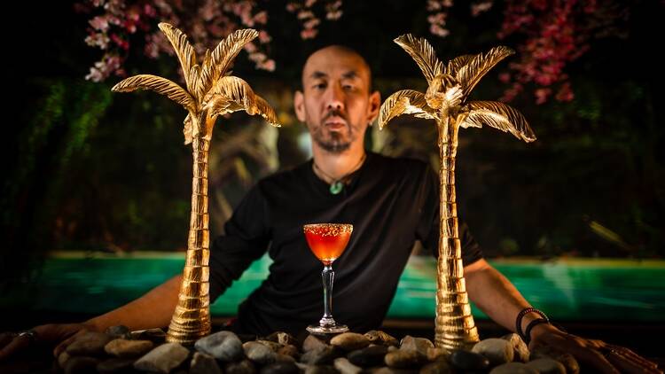 A bartender, a cocktail and two golden palm trees