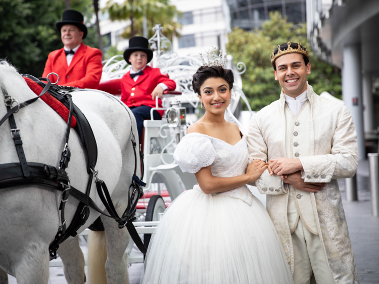 The lead actors playing Cinderella and Prince Charming pose in costume next to a horse drawn carriage