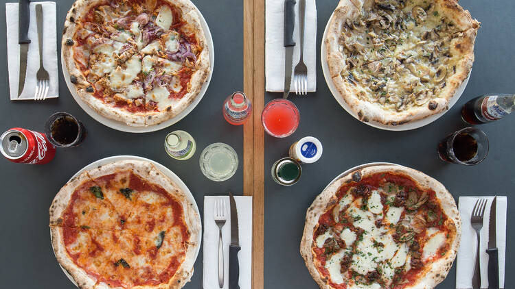 A birds eye view of a table with four table settings with four pizzas and drinks