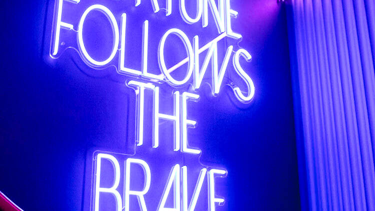 A purple neon sign reading 'fortune follows the brave'.