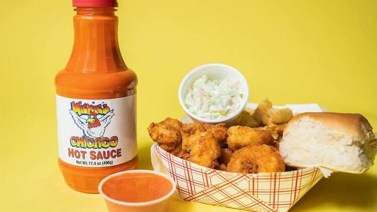 A basket of fried shrimp with coleslaw, a roll and a bottle of hot sauce.