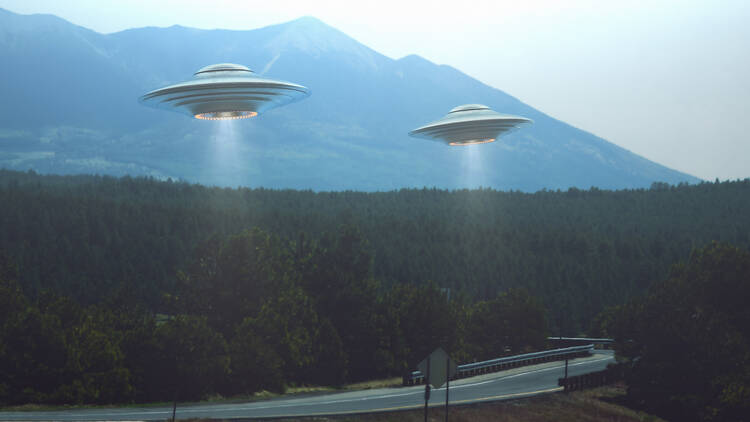 Unidentified flying object. Two UFOs flying over a road among the trees. 3D illustration.