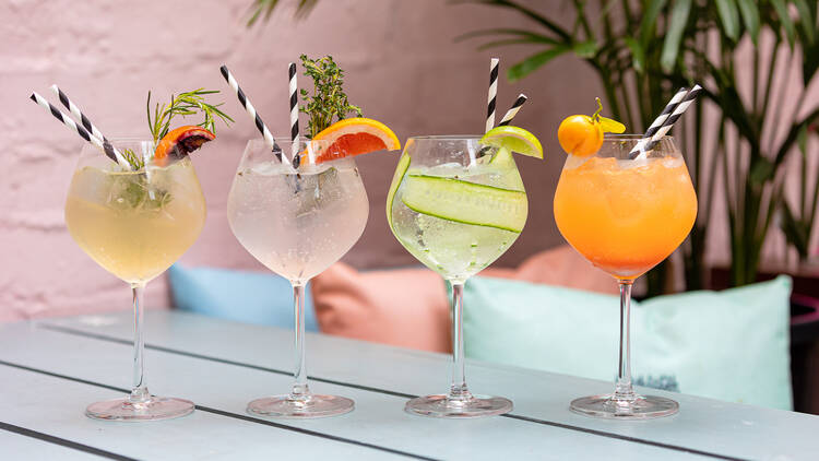 A table in the courtyard has four different cocktails lined up with black and white striped straws