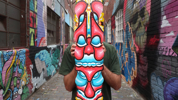 An artist holding a totem pole in a graffiti-covered laneway.