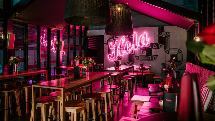 A first-floor bar with pink neon lights and tall bar tables.