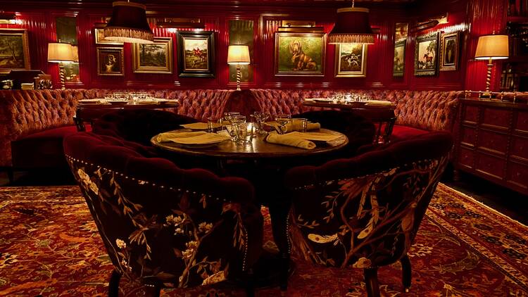 A red room with a table flanked by red velvet dining chairs atop a patterned red rug