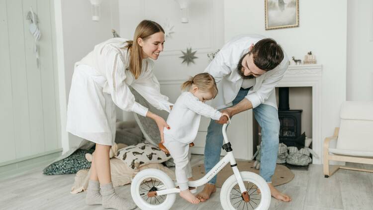 Parents helping their child onto a bicycle.