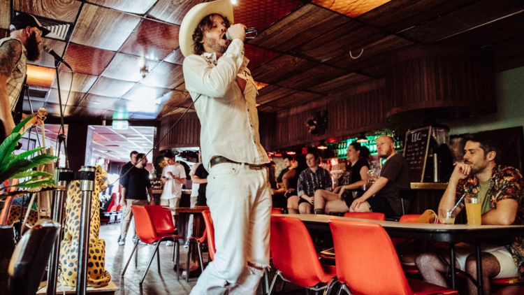 A man sings in a cowboy hat into a microphone 