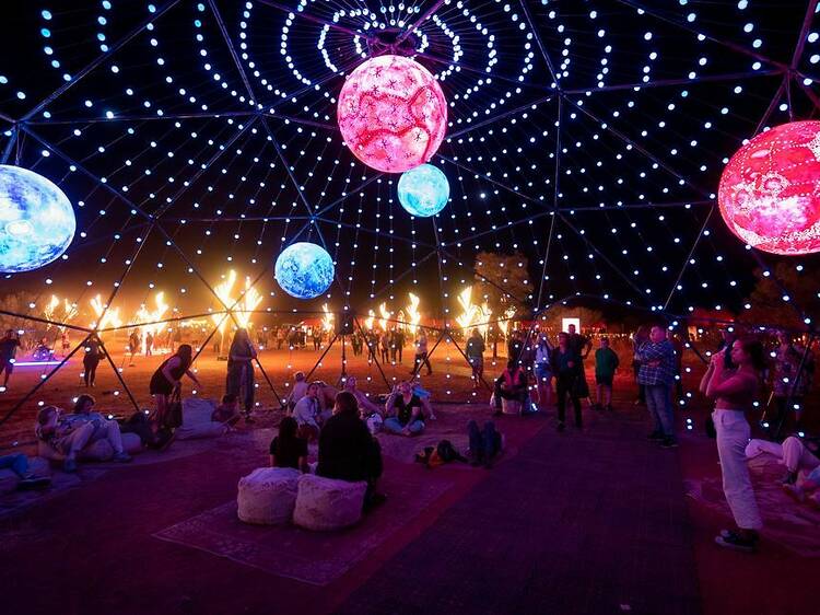 A large see-through igloo with fairy lights, moon-shaped lanterns and people sitting inside.