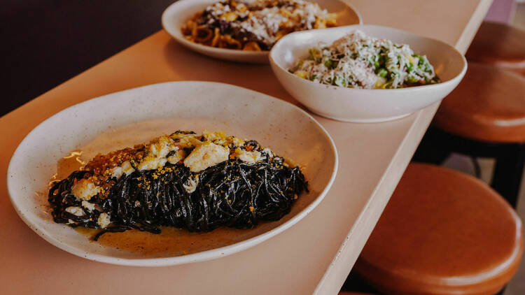 Pink bowls filled with dishes like squid ink pasta.