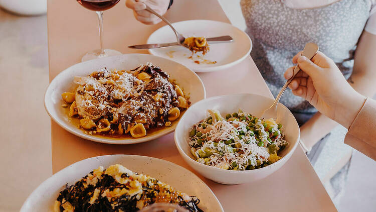 Two women dining at Ragazzone, with pink bowls filled with pasta dishes.