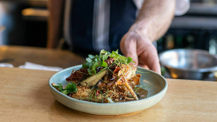 A blue bowl holding a dish topped with cilantro and lemongrass.