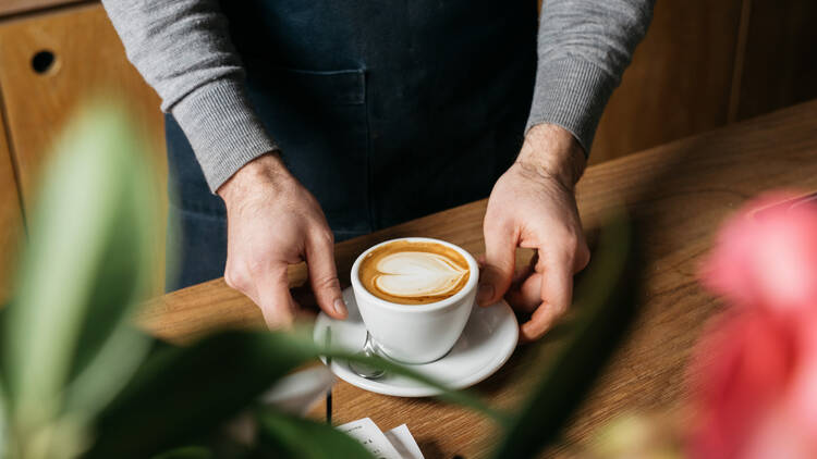 Inside Market Lane Coffee someone places a late in a white mug onto a wooden table