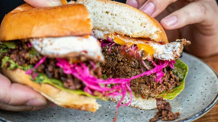 A burger is cut in half on a blue plate which is filled with a patty, an egg and red cabbage