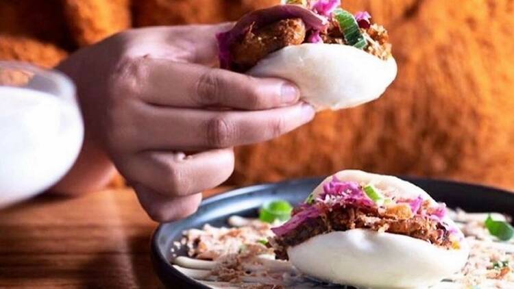 There is a bao on a plate and another bao is being picked up by someone which is filled with meat and vegetables