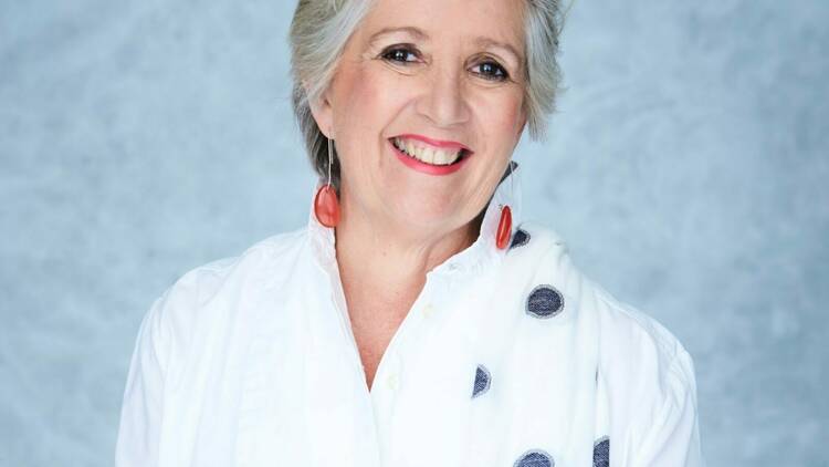 Jane Caro smiling wearing a while shirt and red earrings 