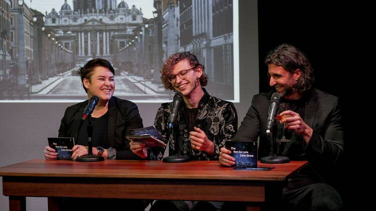 Three performers sit at a table with microphones.