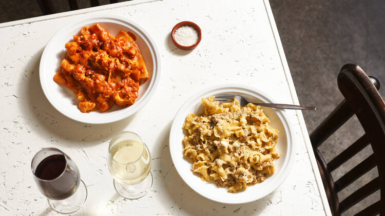 On white table there are two bowls of pasta and two glasses of wine