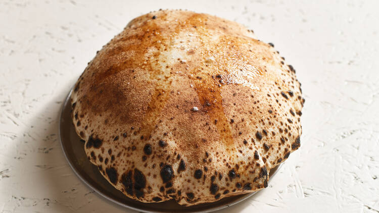 on a white table there is a large piece of woodfired bread out of a pizza oven