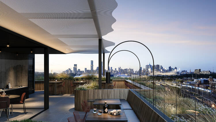 An image of the rooftop restaurant and bar overlooks the city skyline in the background and has tables and chairs and benches