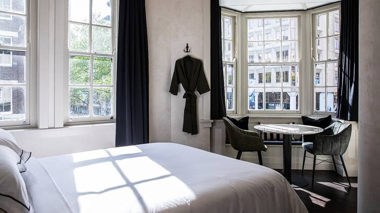 A room in the Strand Hotel with a white bed, green velvet seats and big windows with lots of sunshine