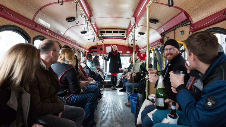 A group of people sitting on a trolley while a tour guide speaks in front