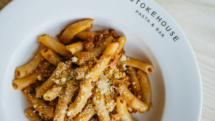 On a white plate the words STOKEHOUSE PASTA AND BAR are printed, and in the bowl it is filled with pasta and ragu sauce