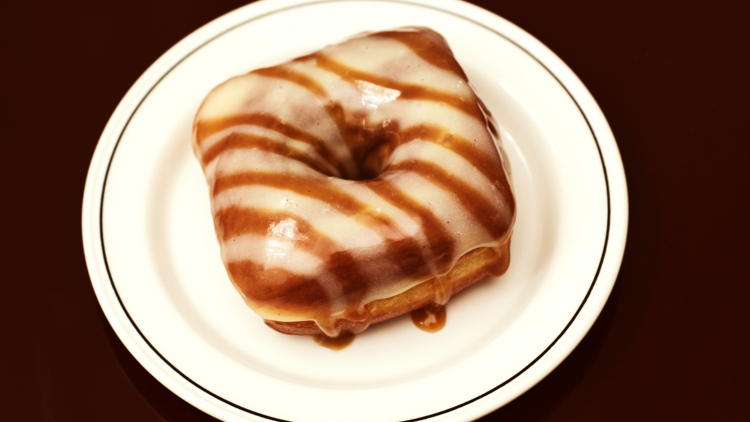 On a white plate there is a donut glazed in white icing with caramel stripes
