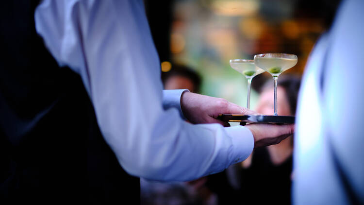 A waiter carries a tray with two martinis on