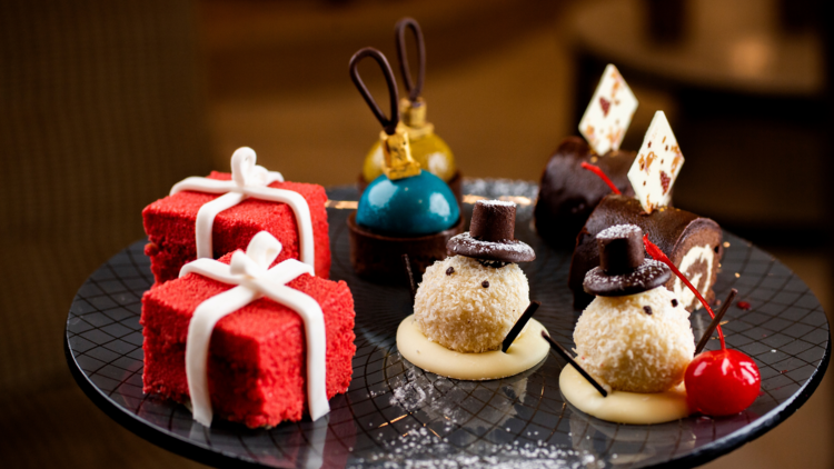 Christmas themed high tea cakes sit on a black platter