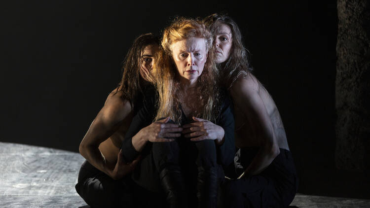 Three women dressed in black snuggle around each other on a stage.