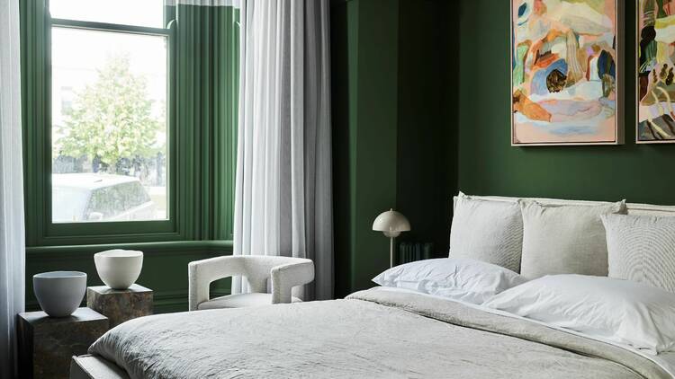 A green-painted interior of a hotel room with a bed, chair and paintings in the room.