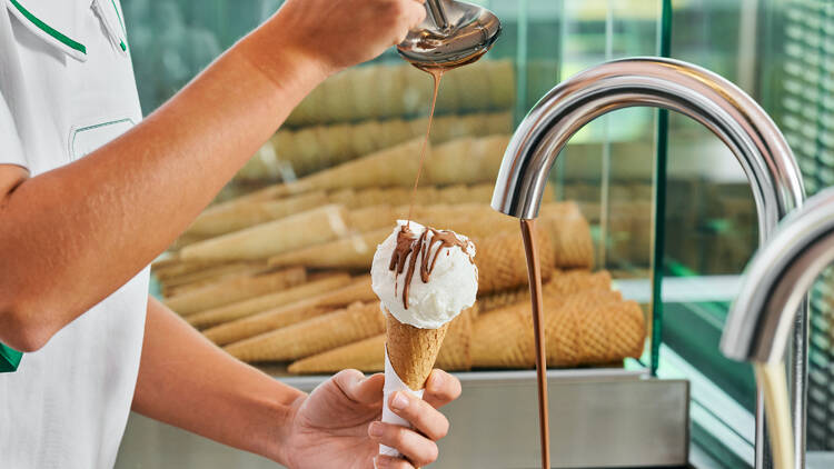 Someone pours chocolate sauce on a cone of gelato 