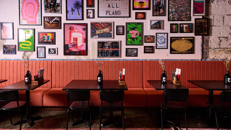 There is a wall filled with framed prints above a red couch and black tables