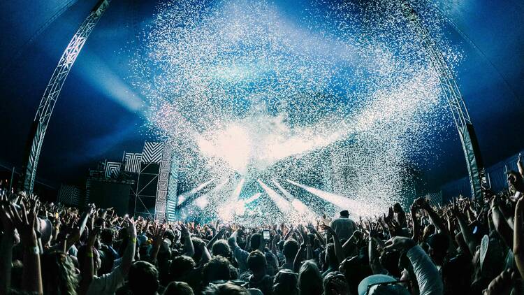 An outdoor music festival stage with a huge crowd of people and laser lights.