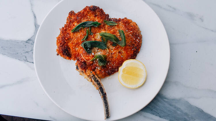 On a large white plate there is a large schnitzel next to a wedge of lemon