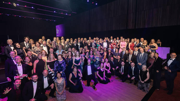A large group of people pose with awards in a ballroom space.