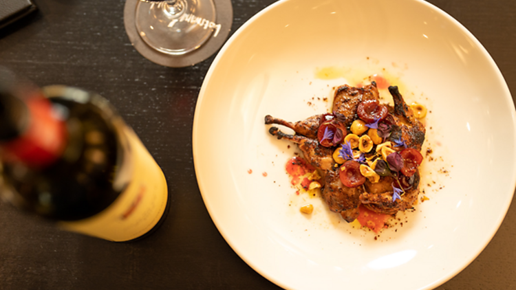 A platter of roast quail next to a bottle and glass of wine.