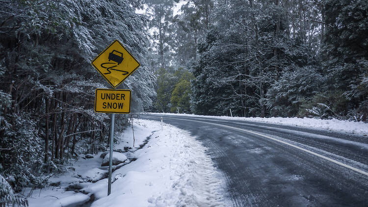 Slippery road warning sign for car drivers on side of a snow covered road.
