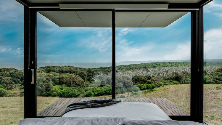 A bed in a glass house overlooking mountains and trees.